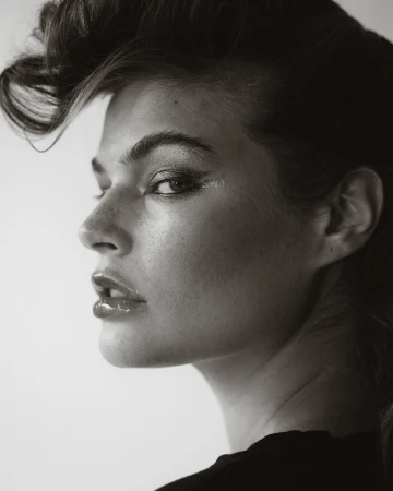 Close-up profile portrait of a woman with styled dark hair and glossy lips in a black and white studio photograph.