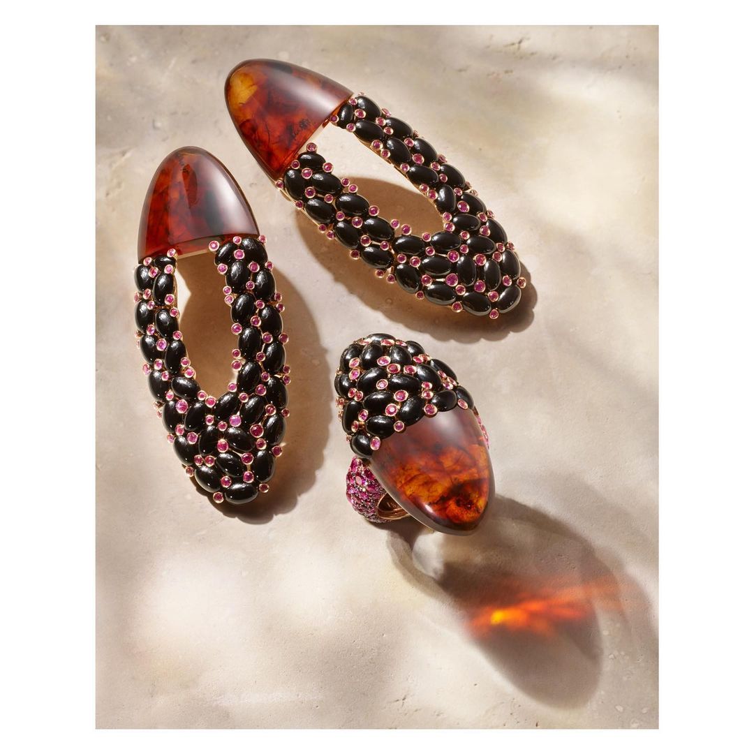 Overhead studio shot of three amber-colored jewelry pieces with interwoven black and pink beaded accents, set against a neutral background.
