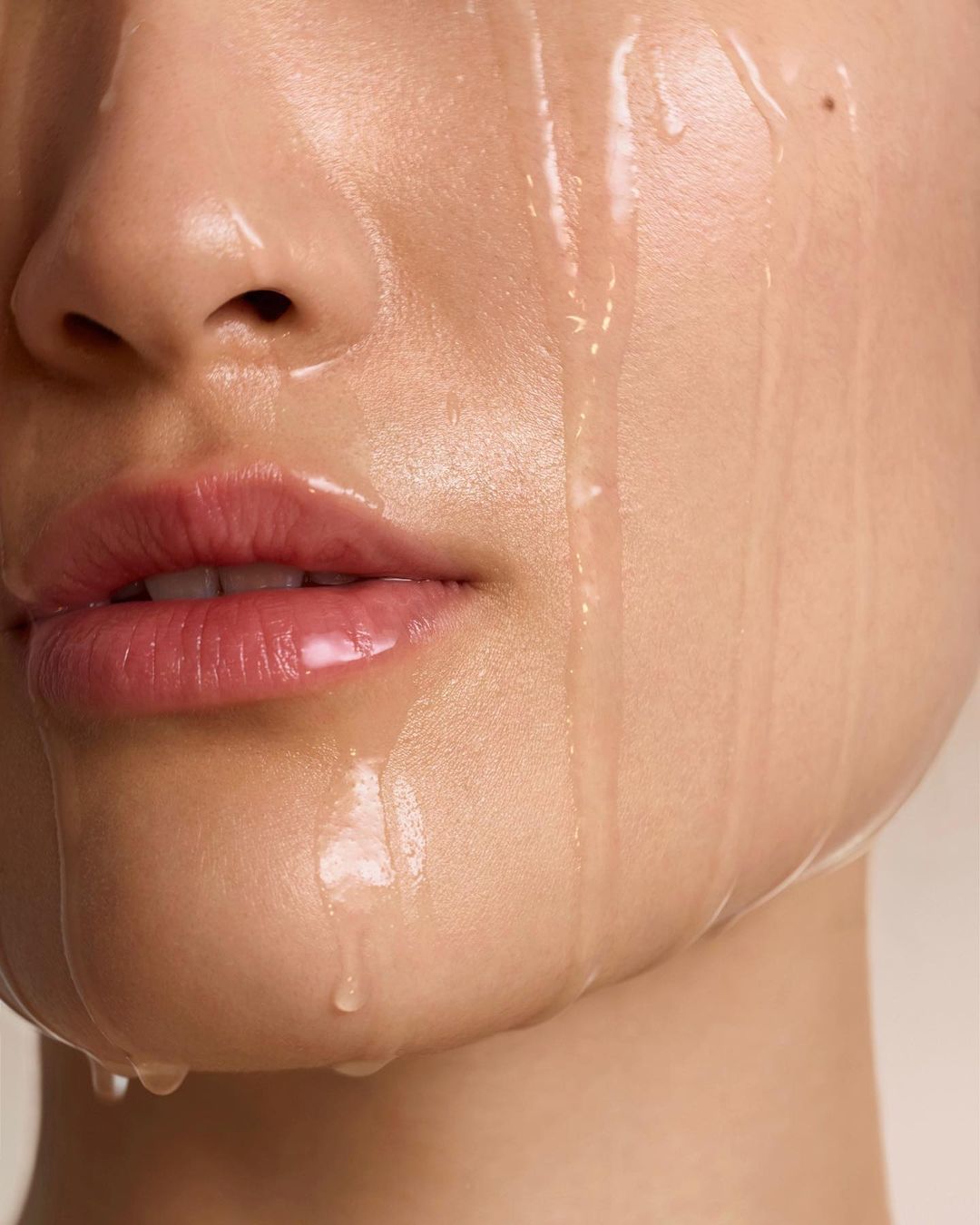Close-up studio shot of a woman's face with water droplets running down her skin, emphasizing skincare and beauty.