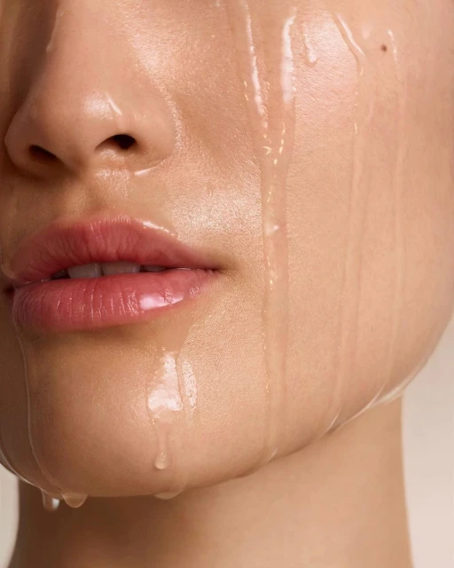 Close-up studio shot of a woman's face with water droplets running down her skin, emphasizing skincare and beauty.