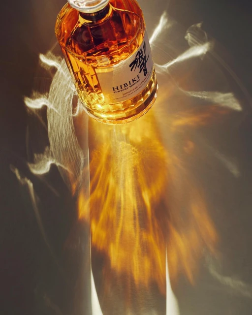 A glass bottle of Hibiki Suntory Whisky sits indoors, casting warm light and reflections on a smooth surface with neutral coloring.