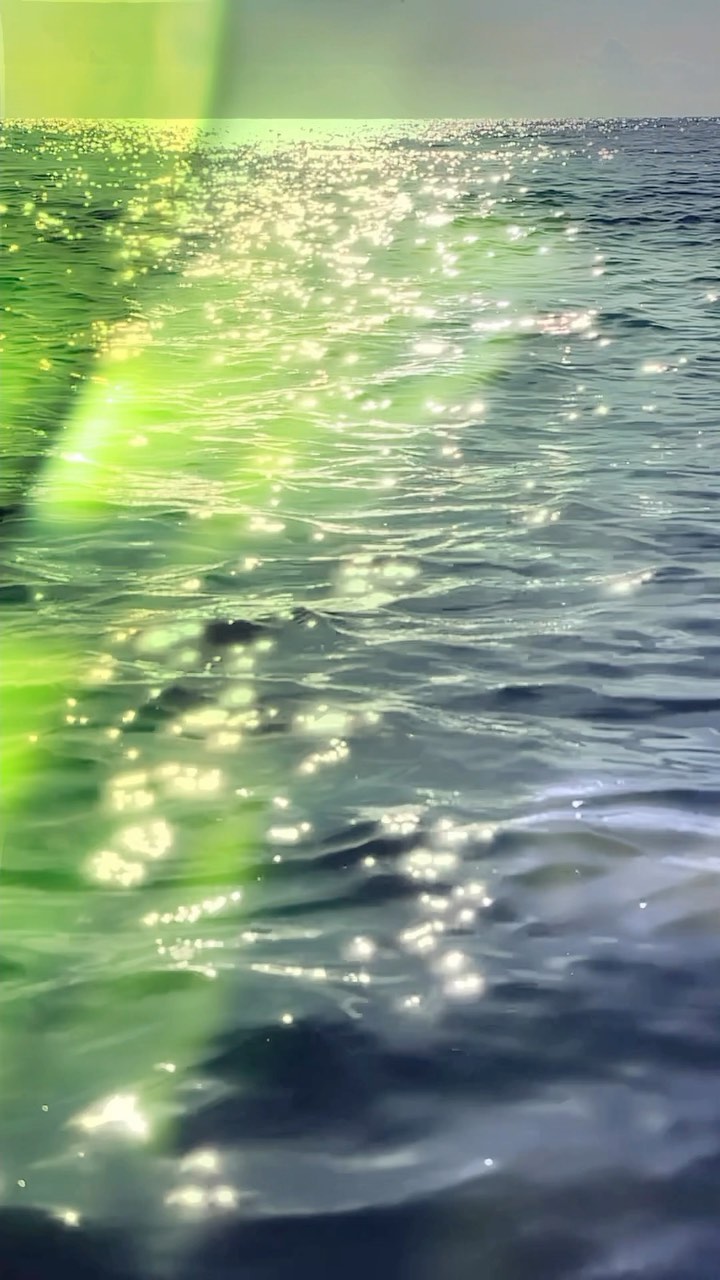 Sunlight glimmers on a vast, rippling ocean expanse, creating a mesmerizing display of light and water reflections.