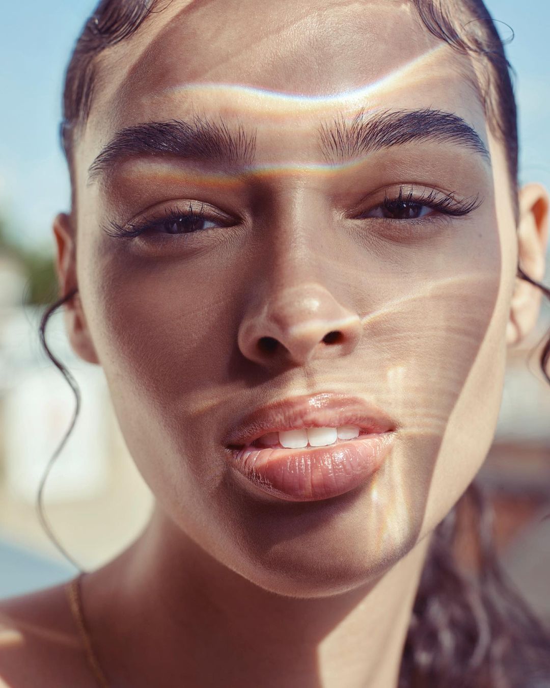 Close-up portrait of a woman with natural light casting prismatic refractions and shadows across her face.