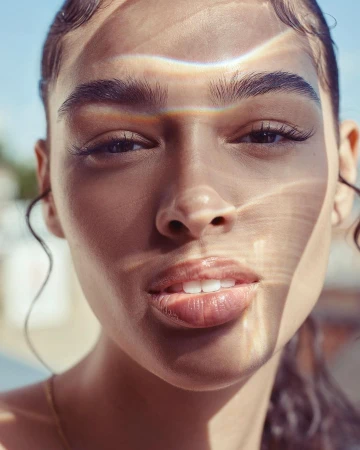 Close-up portrait of a woman with natural light casting prismatic refractions and shadows across her face.