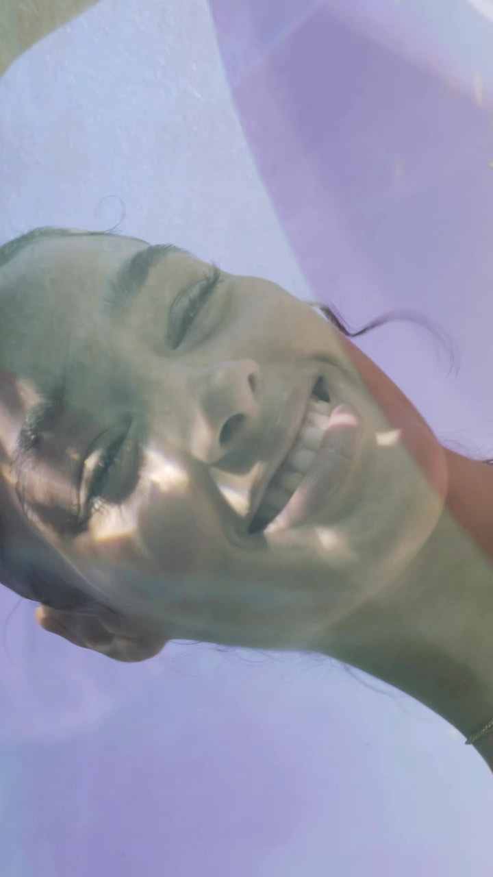 Portrait of smiling woman with light and shadow patterns on her face, dreamy purple background, natural lighting, looking up.
