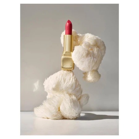 Elegant pink lipstick by Guerlain sitting on a fluffy white prop against a soft gray background in a beauty product shot.