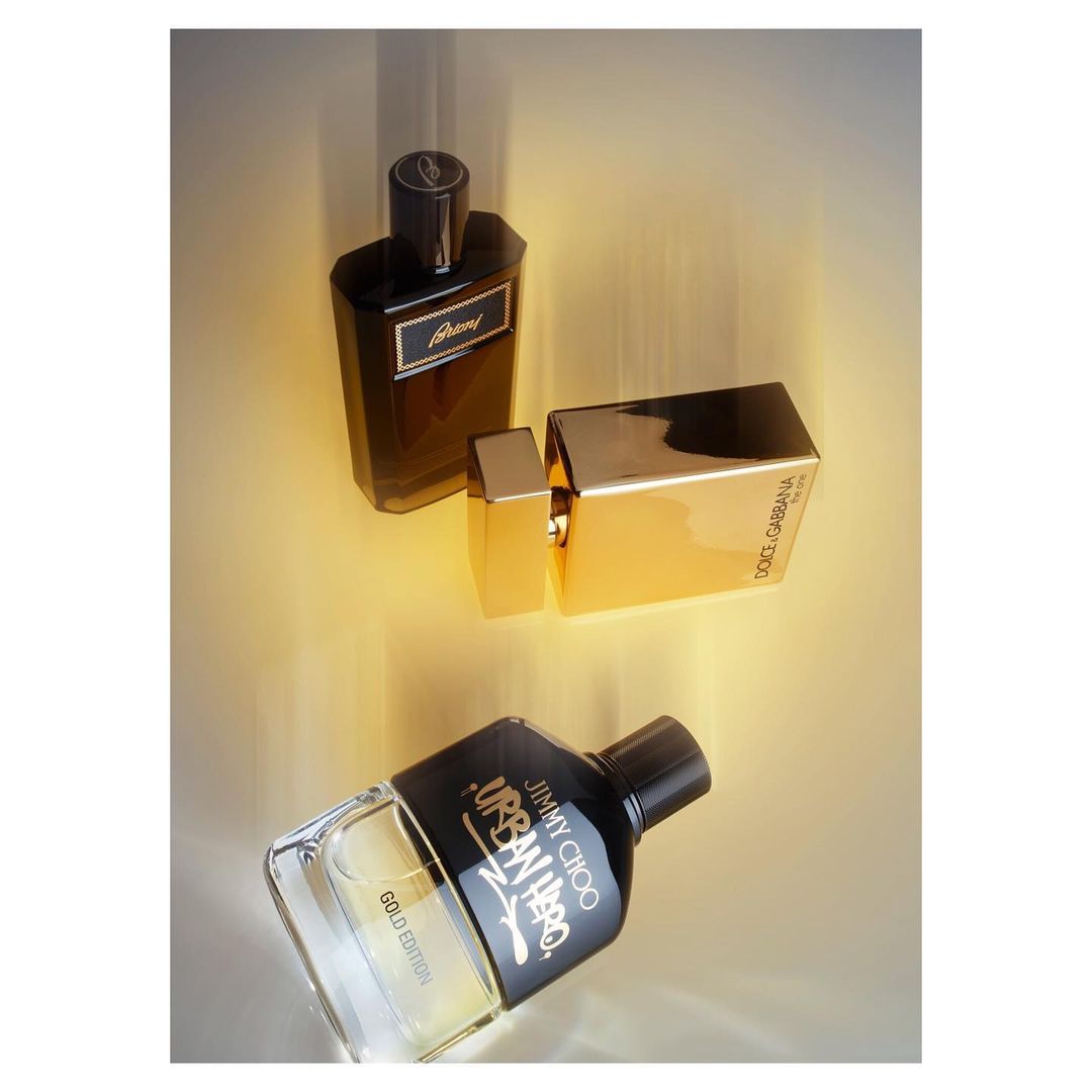 Three glass perfume bottles with black caps are displayed on a reflective surface in a studio, highlighted by soft, diffused lighting.