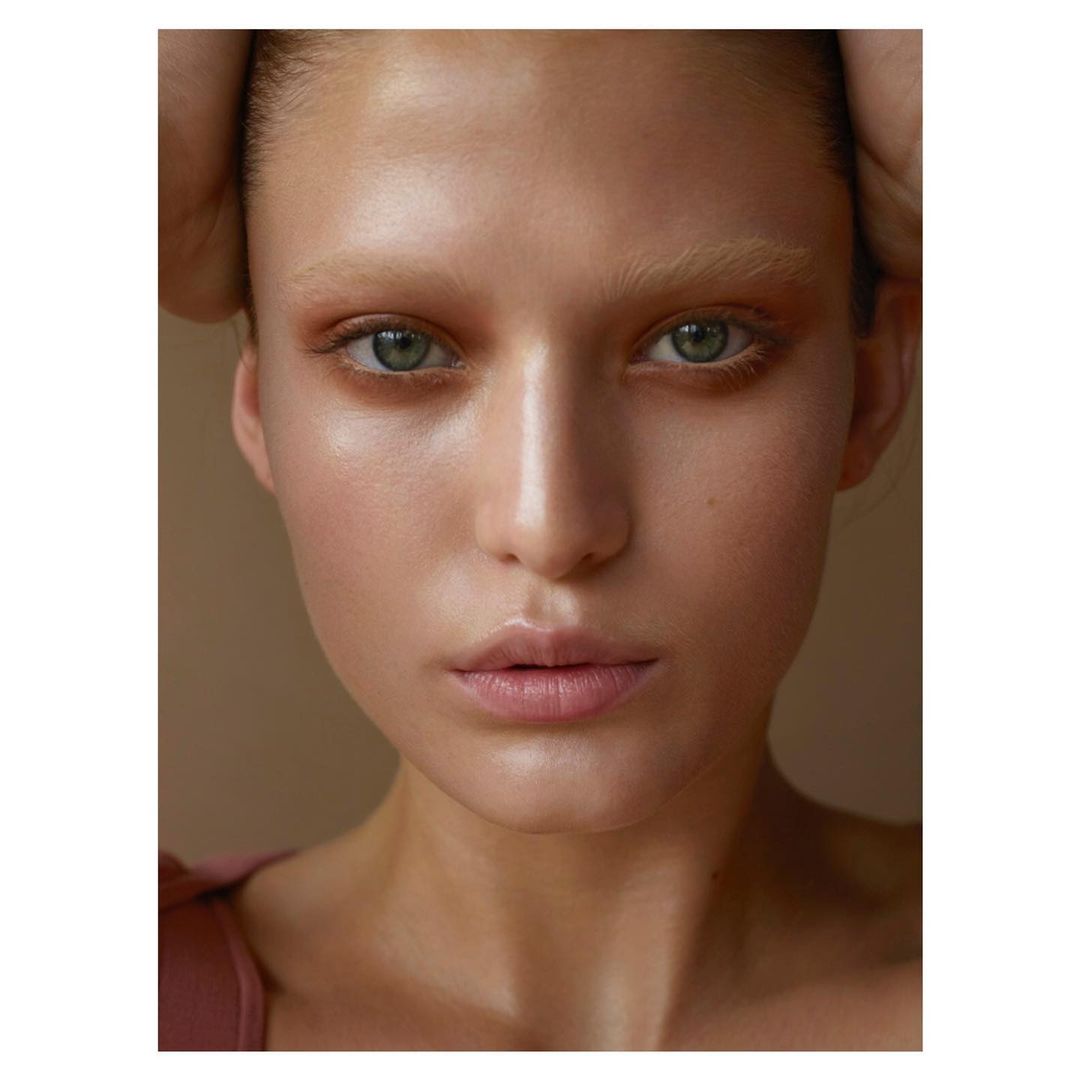 Close-up studio portrait of a young adult female with fair skin, light green eyes, neutral expression, hands framing the face, and soft lighting.