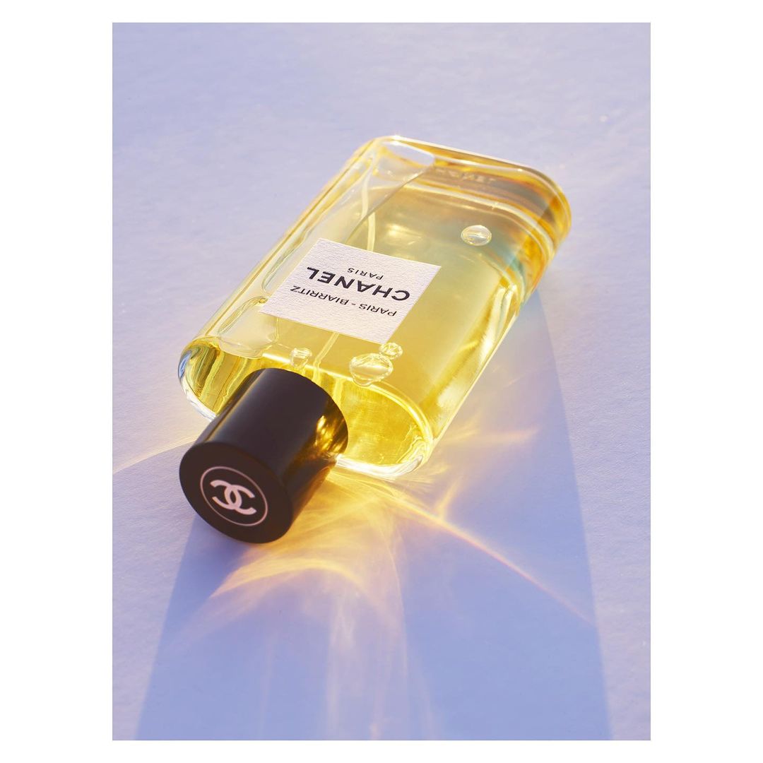 Angled shot of a clear Chanel Paris-Biarritz perfume bottle with a black cap on a smooth surface, creating a clean and minimalist aesthetic.