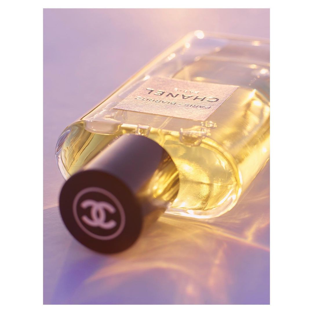 Close-up of a Chanel perfume bottle with a black cap displaying the interlocking C logo, set against a soft, diffused lighting background.