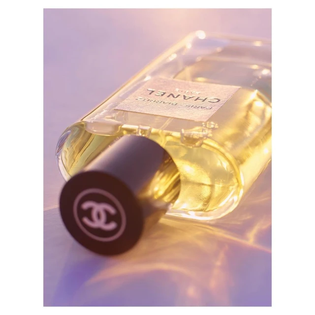 Close-up of a Chanel perfume bottle with a black cap displaying the interlocking C logo, set against a soft, diffused lighting background.