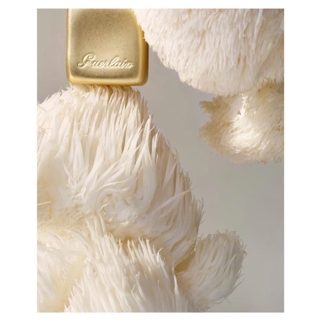 Close-up of a golden perfume bottle with the Guerlain logo, topped with fluffy white feathers, creating a soft and luxurious aesthetic.
