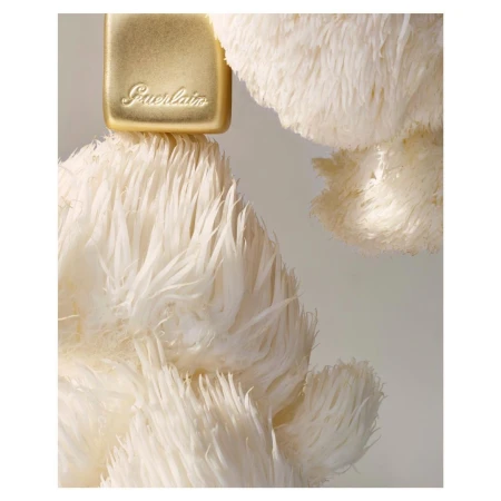 Close-up of a golden perfume bottle with the Guerlain logo, topped with fluffy white feathers, creating a soft and luxurious aesthetic.