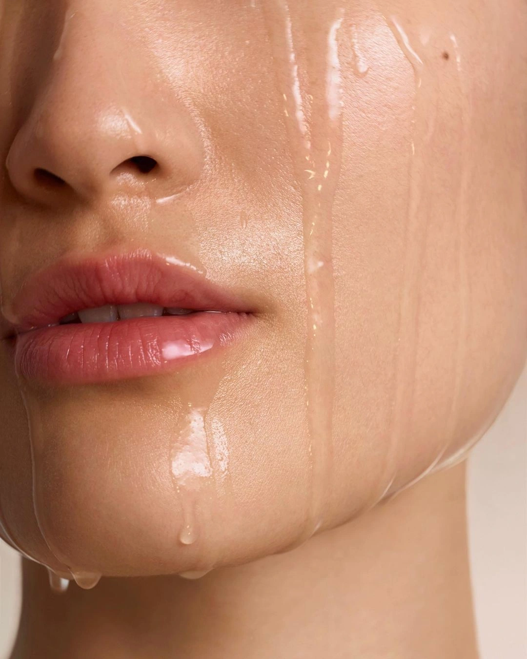 Extreme close-up of a person's lower face with glistening liquid dripping down skin and lips photographed by Karin Berndl.