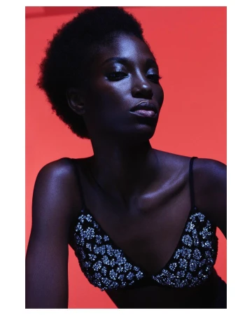 Portrait of a Black woman in a sequin bralette against a vivid red background, photographed by Karina Twiss in Paris.