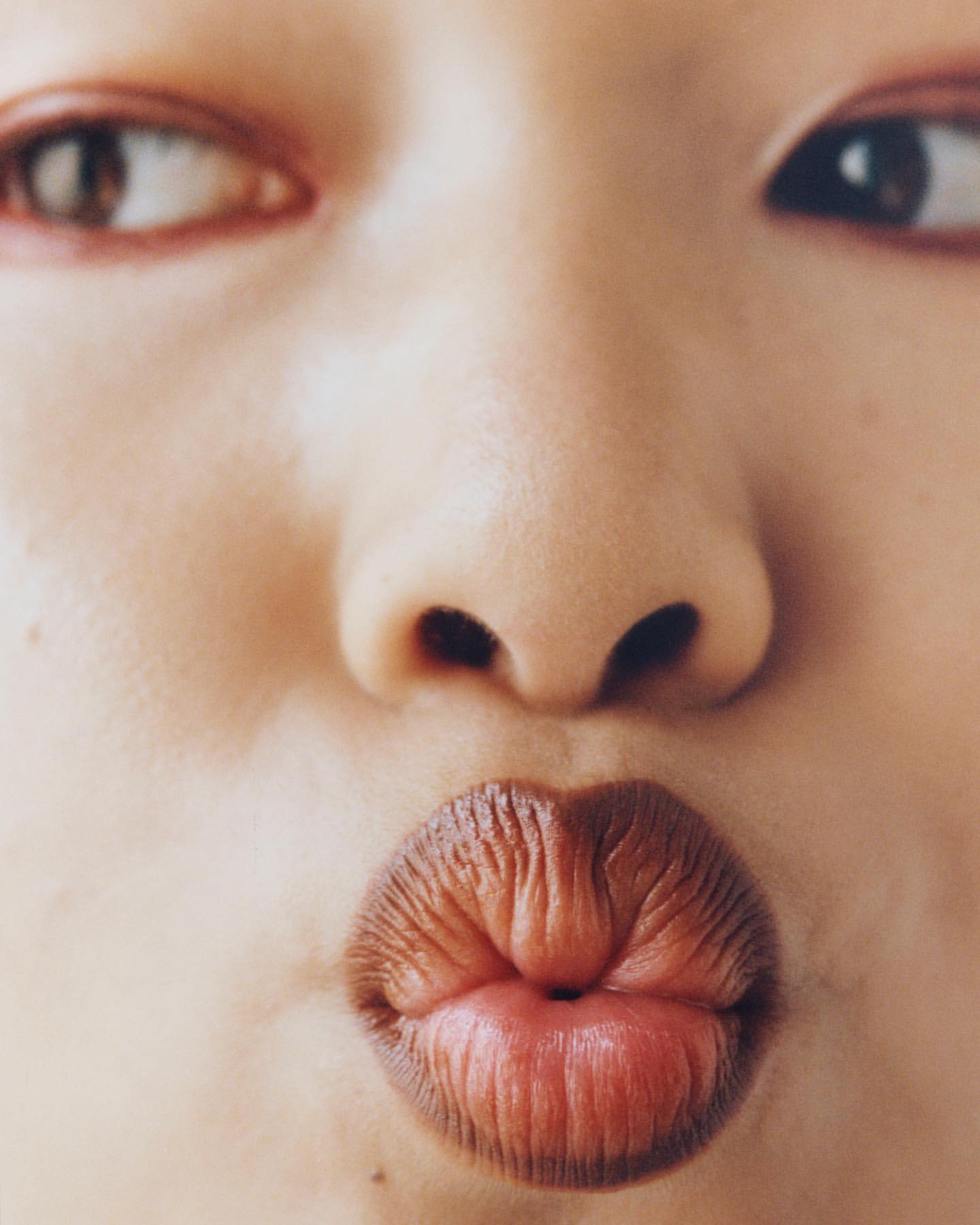 Close-up of a young person's face with puckered lips, fair skin, and eyes looking off to the side. The focus is on the expression.