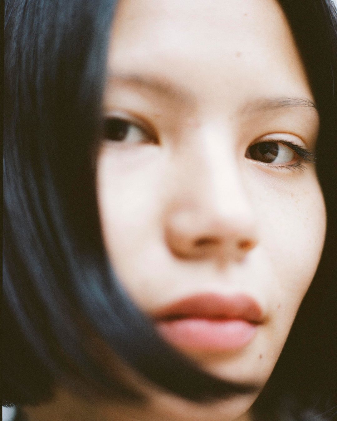 Close-up portrait of a young woman with dark hair, fair skin, and neutral expression, focusing on facial details and soft lighting.