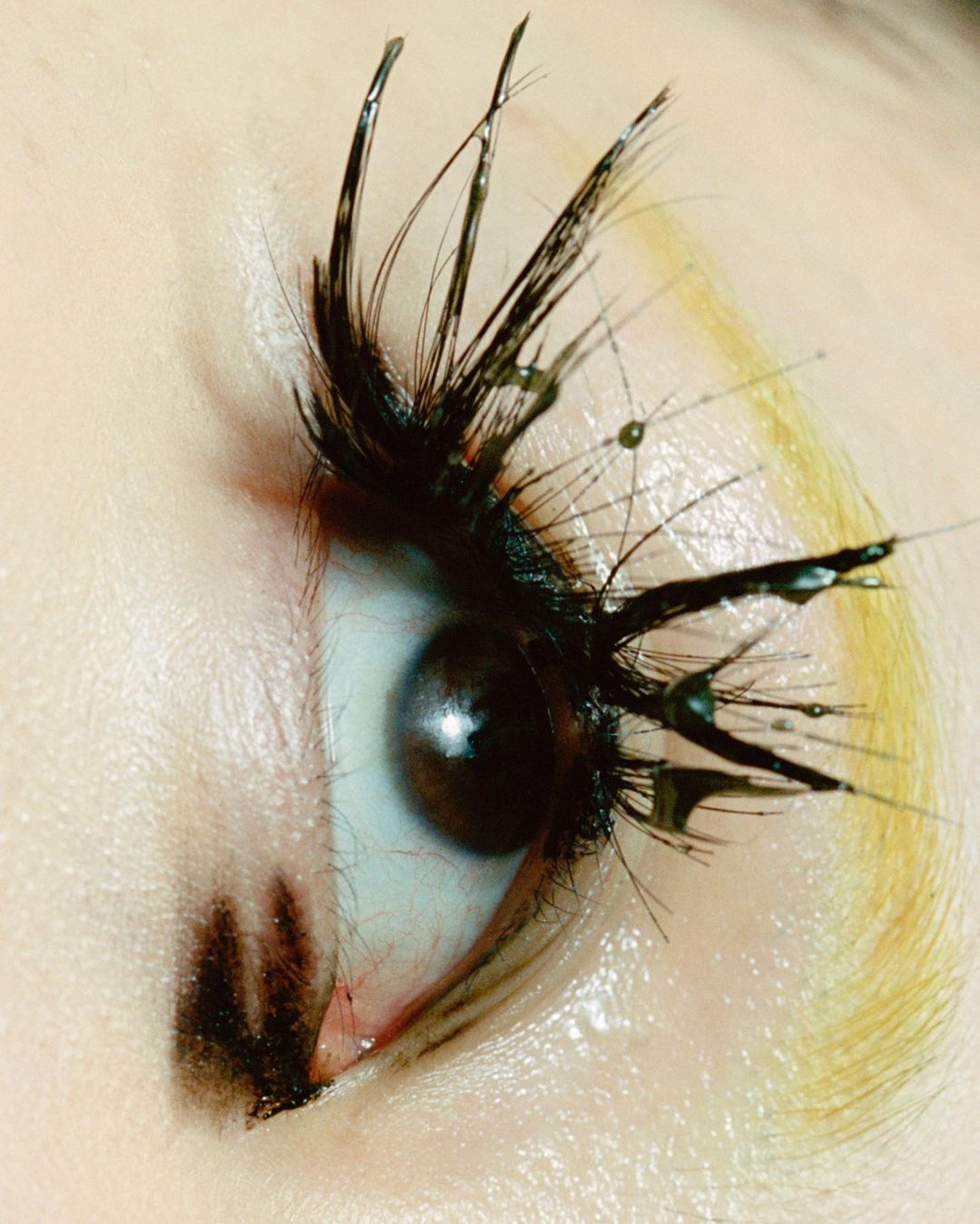 Macro beauty shot of a brown eye with creative mascara forming spikey lashes with water droplet details, artistic makeup and presentation.