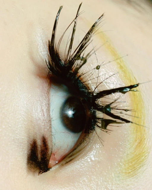 Macro beauty shot of a brown eye with creative mascara forming spikey lashes with water droplet details, artistic makeup and presentation.