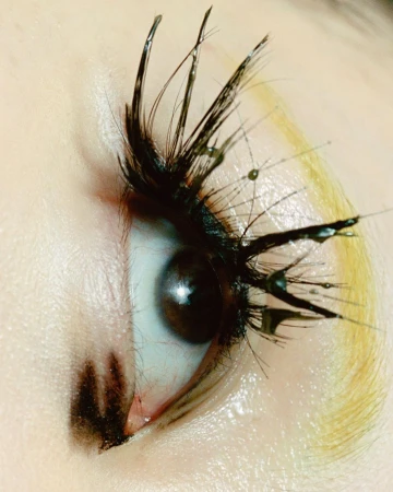 Macro beauty shot of a brown eye with creative mascara forming spikey lashes with water droplet details, artistic makeup and presentation.