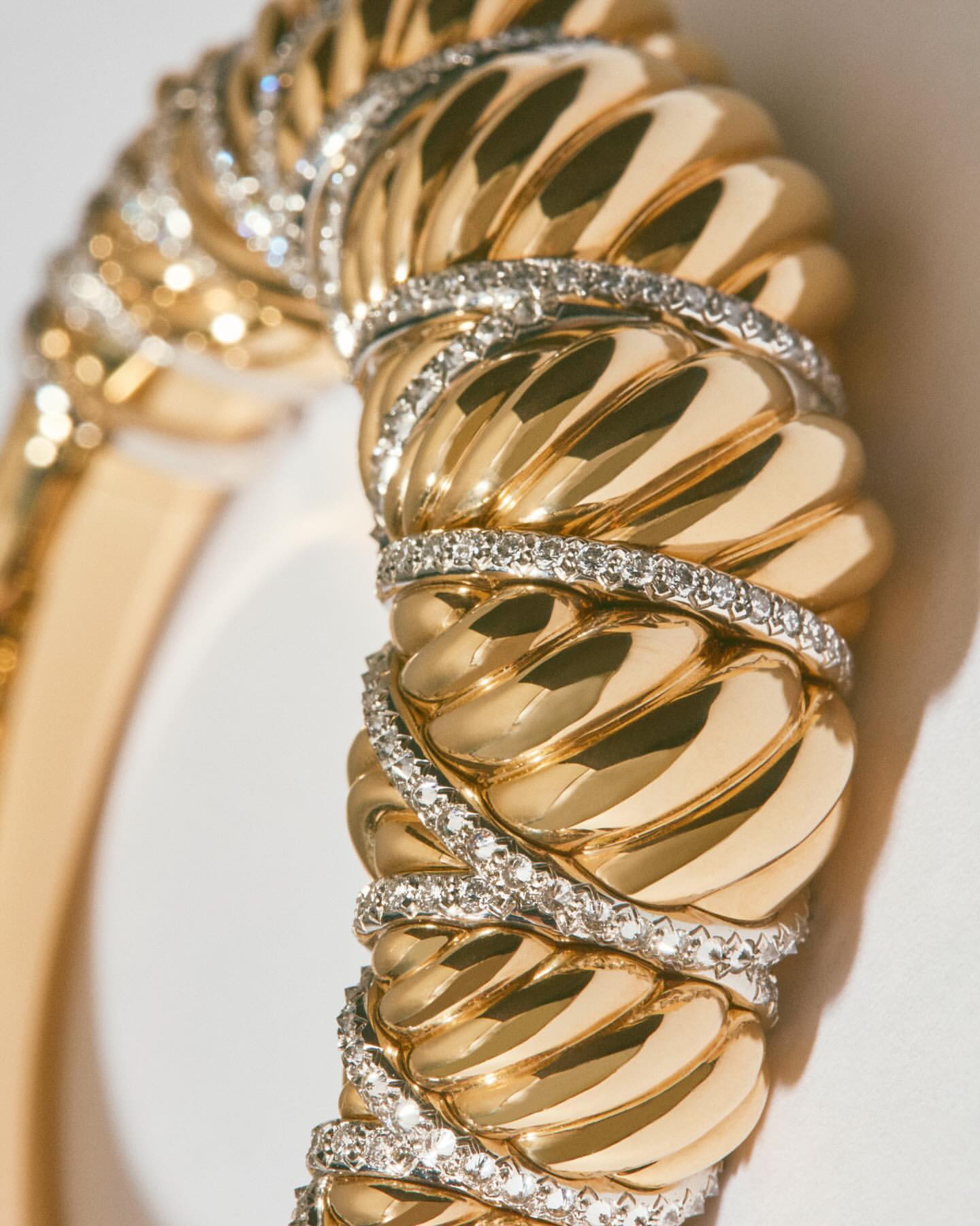 Close-up of a luxurious gold bangle bracelet adorned with diamond accents, showcasing its intricate design and sparkling details against a soft background.