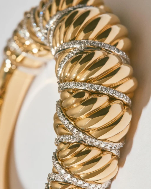 Close-up of a luxurious gold bangle bracelet adorned with diamond accents, showcasing its intricate design and sparkling details against a soft background.
