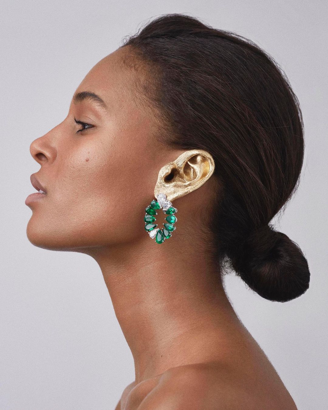 Profile shot of an adult female wearing green gemstone earrings. The earrings are attached to a gold-toned ear-shaped structure.