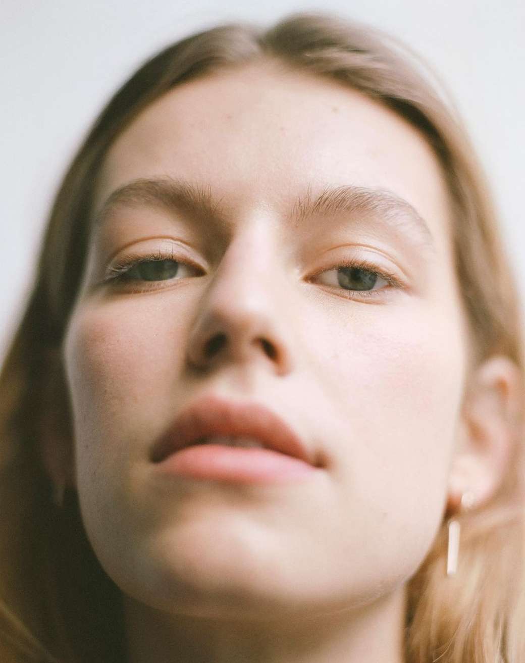 Extreme close-up portrait of a woman looking down at camera with natural lighting against a plain white background