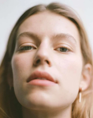 Extreme close-up portrait of a woman looking down at camera with natural lighting against a plain white background