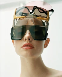 Close-up portrait of a woman wearing multiple stacked pairs of designer sunglasses on her head by photographer Karina Twiss.