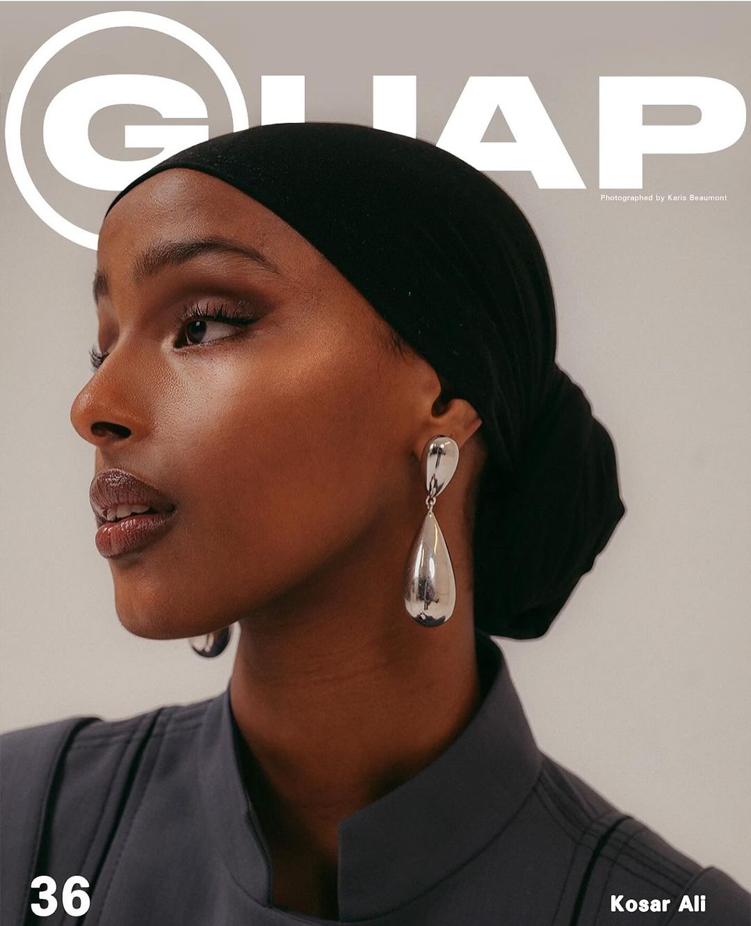 Close-up portrait of a woman with dark hair, wearing a black headscarf and silver teardrop earrings, against a neutral background for a magazine cover.