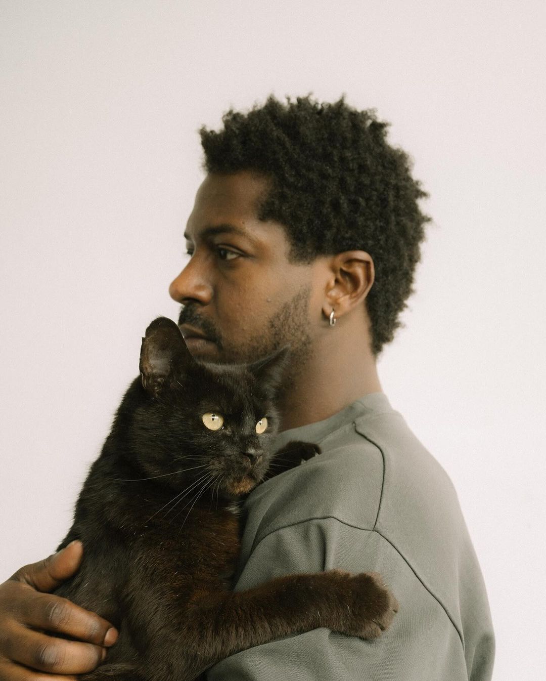 Portrait of a young adult man holding a black cat against a white backdrop, focusing on their close interaction and contrasting colors.