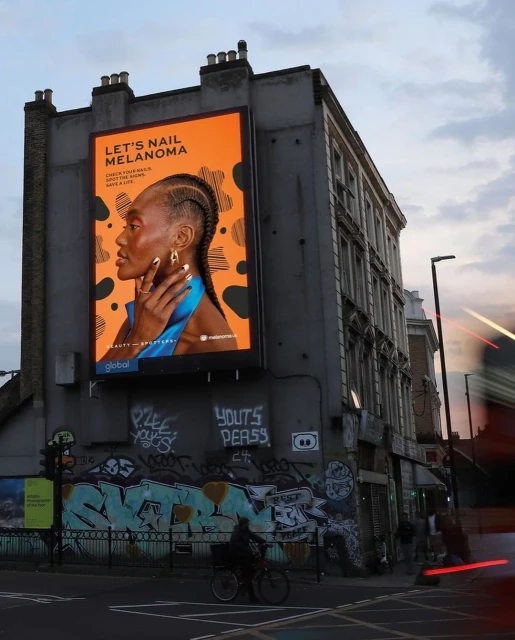Beauty ad on an urban building features a woman with braided hair and stylish nails against a bright orange and black backdrop.