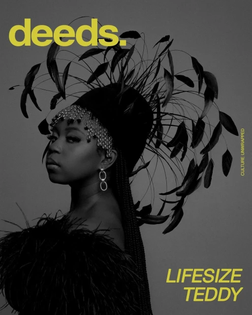 Black and white magazine cover shot of a woman wearing feathered headpiece and shoulder covering against a gray backdrop.