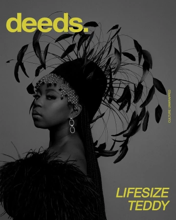 Black and white magazine cover shot of a woman wearing feathered headpiece and shoulder covering against a gray backdrop.