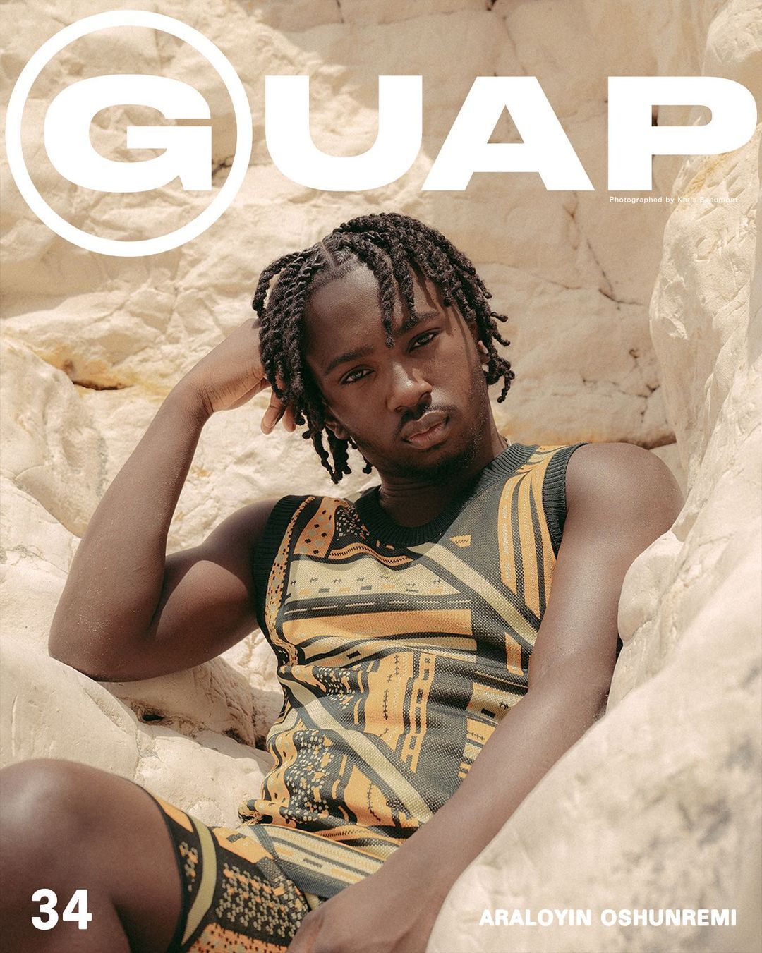 Magazine cover featuring a young man with braided hair, wearing a patterned outfit, sitting in front of a rocky background. Bold text at the top.