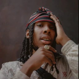 Portrait of a Black man with dreadlocks wearing a patterned headwrap and textured jacket, captured by photographer Karis Beaumont.