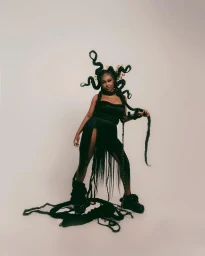Black woman with intricate sculptural braided hair standing in a black outfit against a plain light background