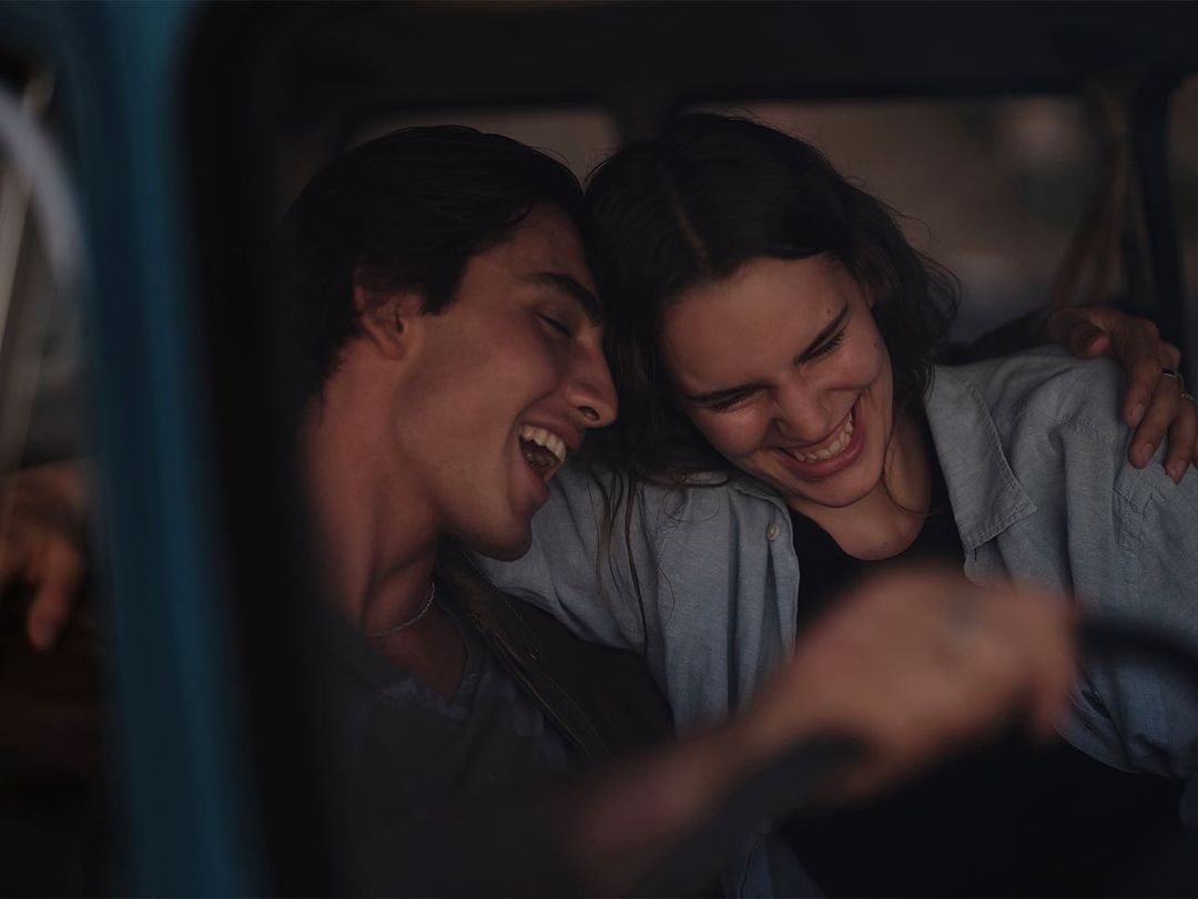 Close-up portrait of a laughing young man and woman sitting together inside a vehicle, photographed by Kate Abbey.