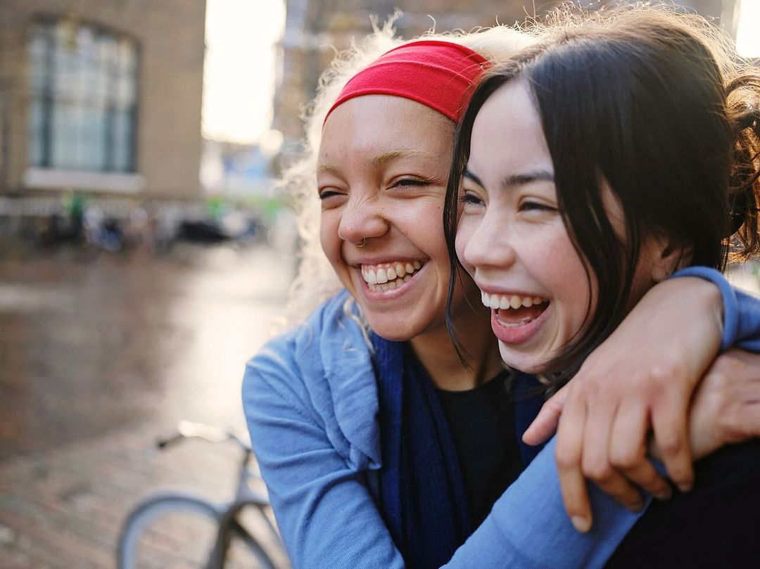 Two young women share a joyful moment outdoors, embracing each other and laughing with genuine happiness in natural light.