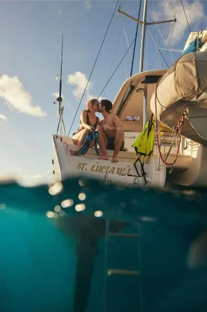 A couple kisses on the stern of a sailboat, with the boat partially submerged, capturing the waterline and the underwater view.