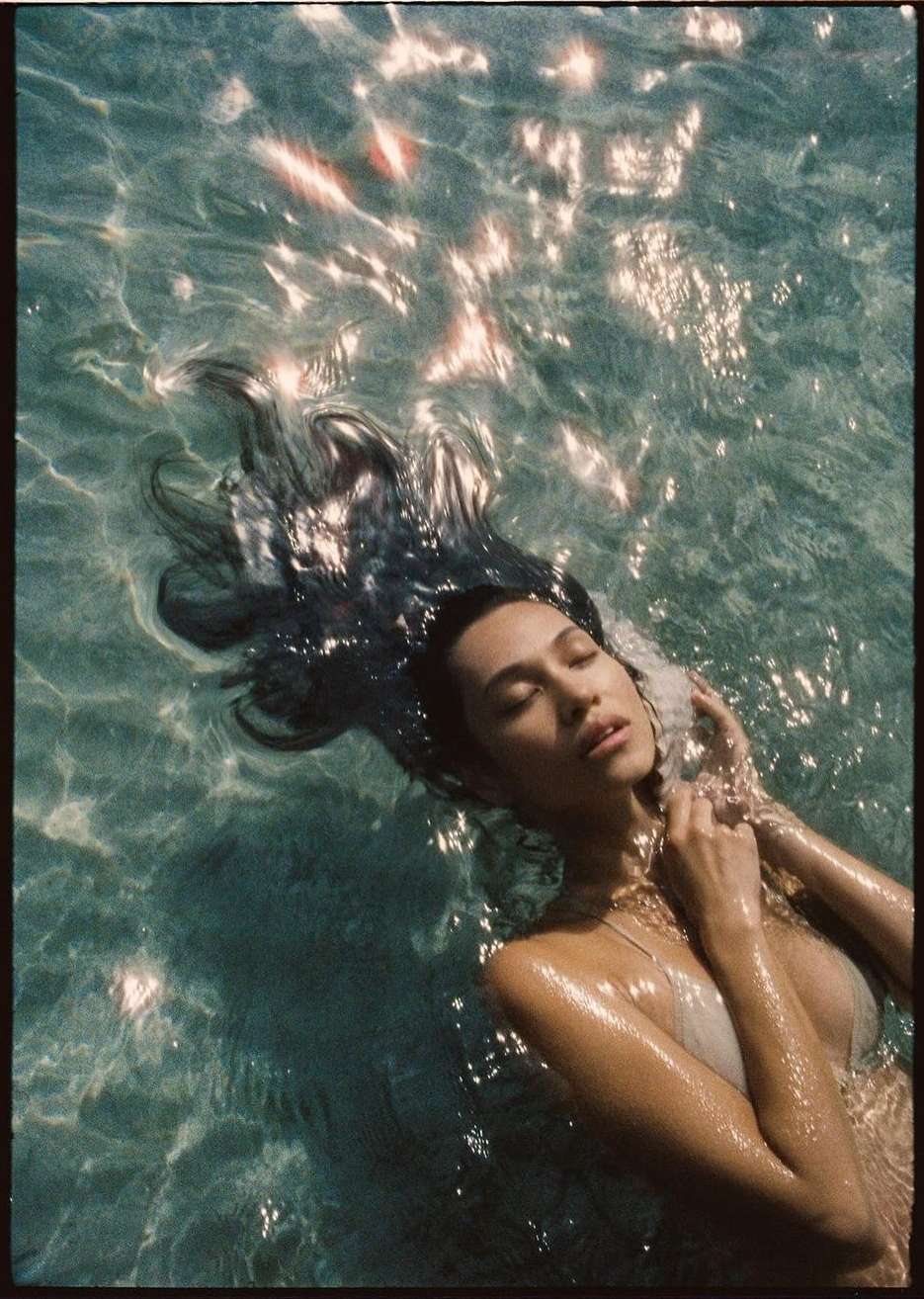 Woman floating in crystal-clear water with sunlight glinting on the surface, captured by Kate Bellm