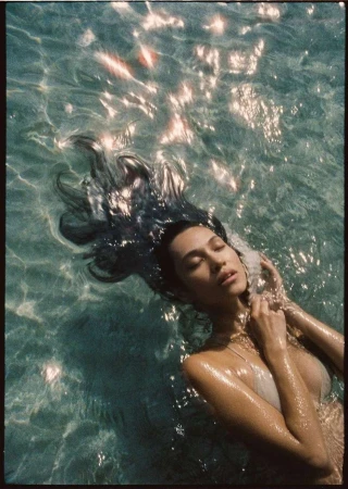 Woman floating in crystal-clear water with sunlight glinting on the surface, captured by Kate Bellm