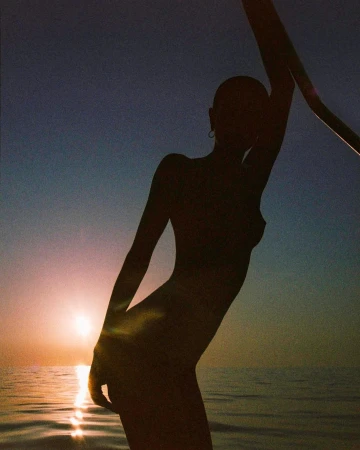 Silhouette of a person leaning against a railing against a sunset sky over the ocean