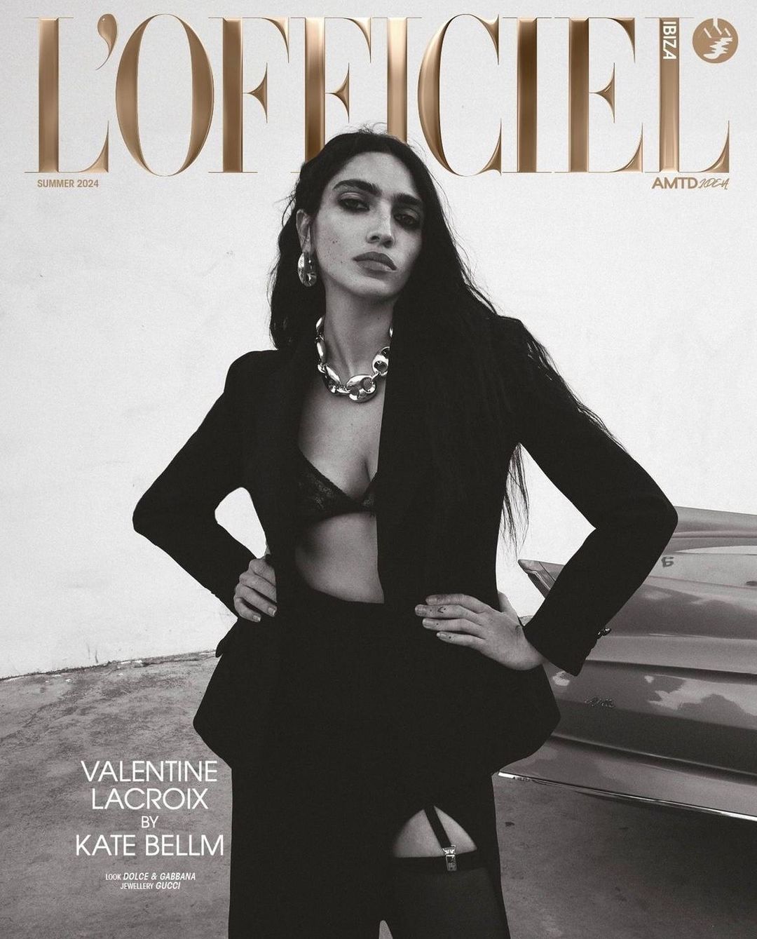 L'Officiel Ibiza Summer 2024 cover featuring a woman in a black blazer, bralette, and stockings, posing with hands on hips near a car.