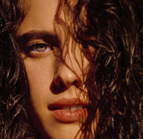 Close-up portrait of a woman with wet dark hair across her face and striking blue eyes by Kate Bellm