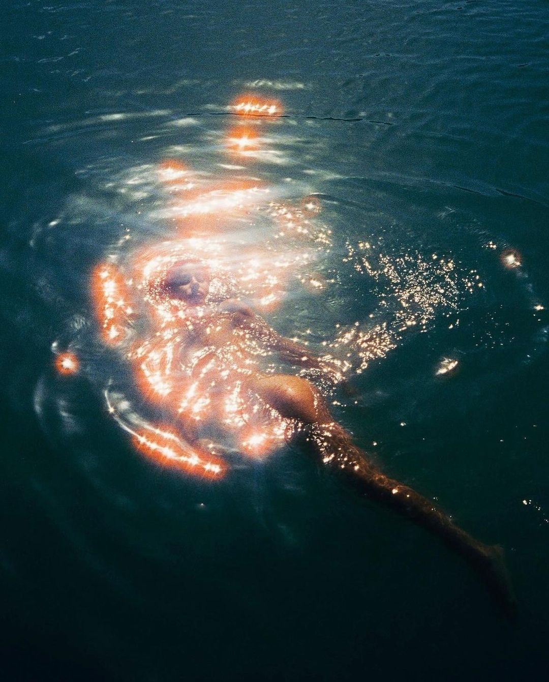 Woman swims in the ocean with shimmering sunlight reflecting on the surface of the water, creating a bright and ethereal scene.