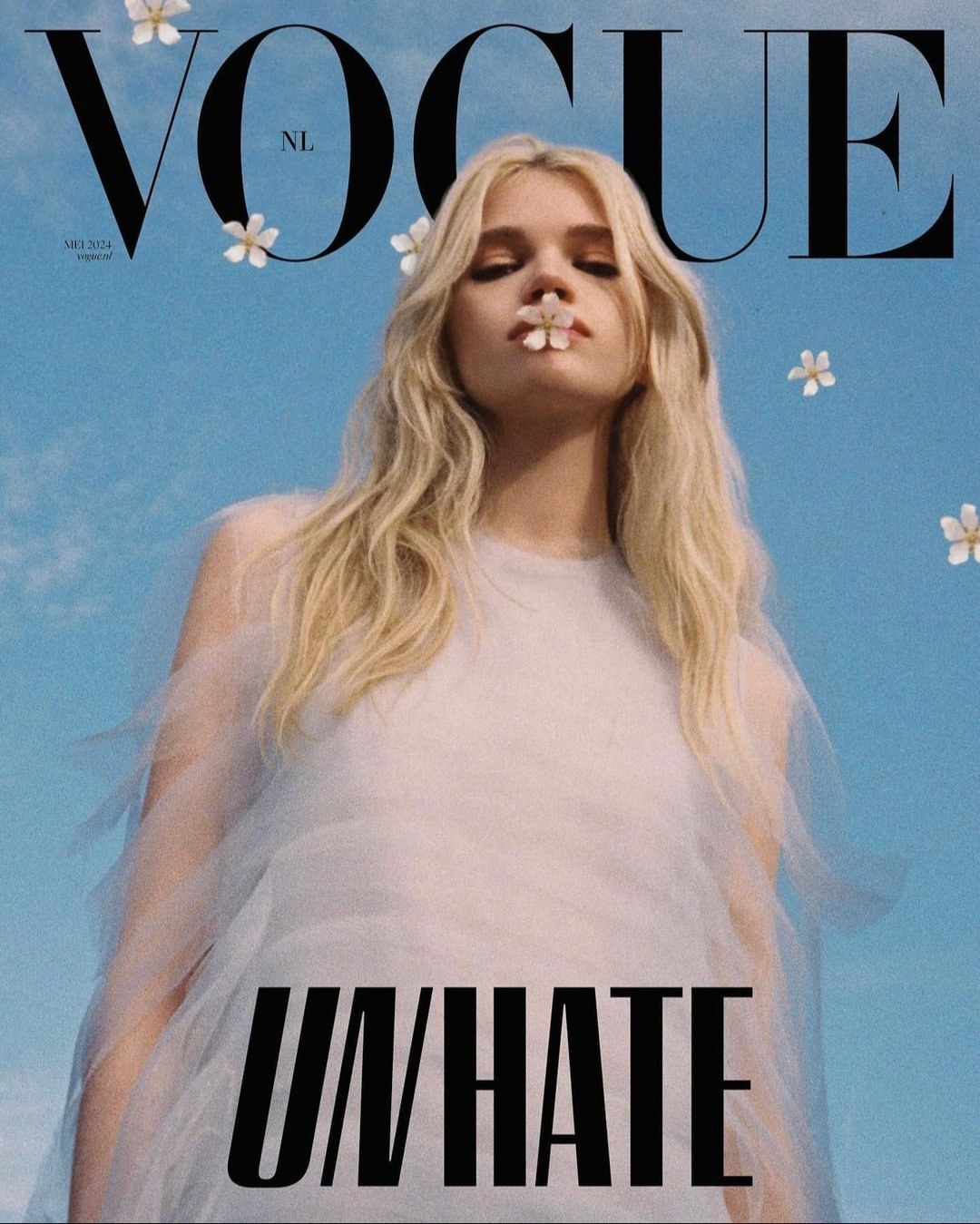 Vogue NL cover featuring a blonde woman in a white dress with small flowers in her hair and one in her mouth against a blue sky.