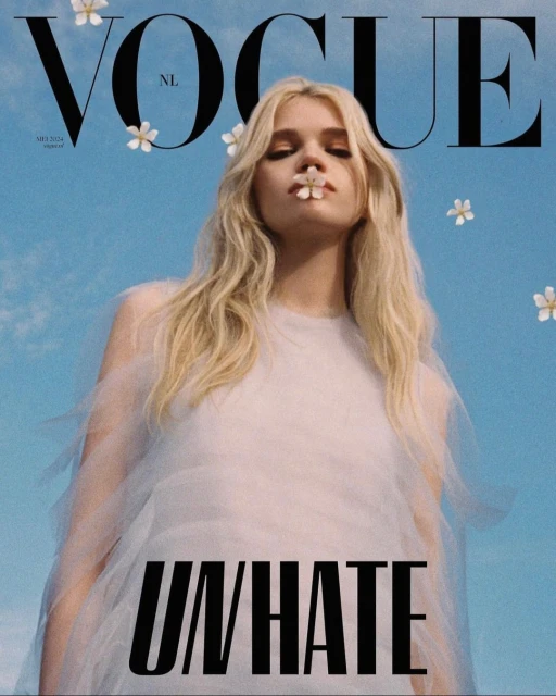Vogue NL cover featuring a blonde woman in a white dress with small flowers in her hair and one in her mouth against a blue sky.