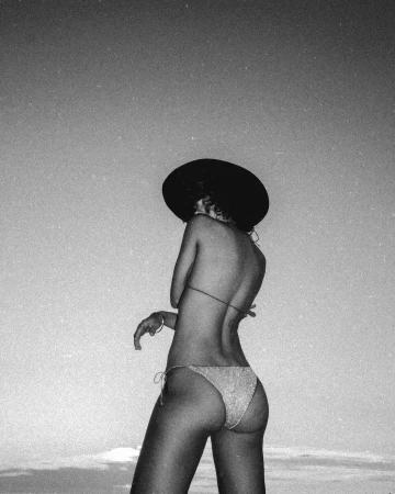 Monochrome film photograph of a woman in a bikini and wide-brim hat against a clear sky